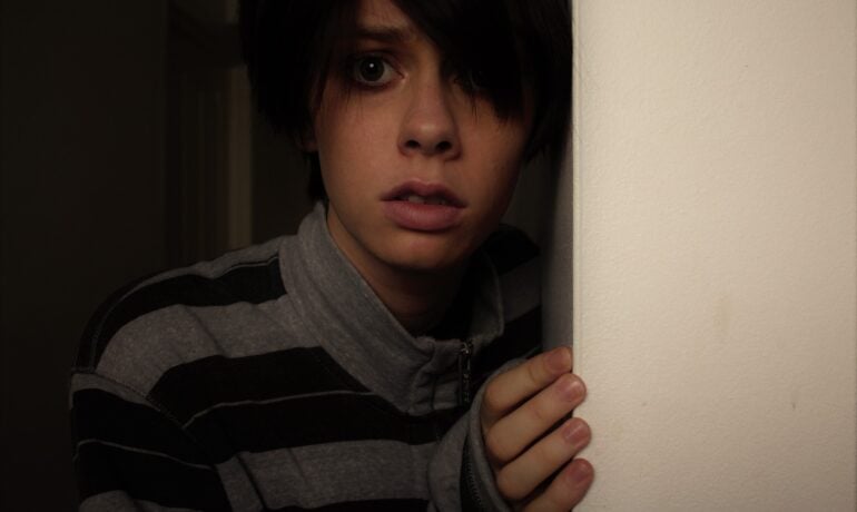 młoda osoba, która się boi stojąca przy ścianie