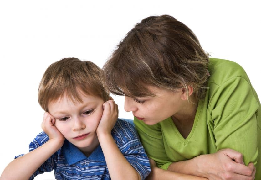 kobieta mówiąca do dziecka podpierającego głowę rękami