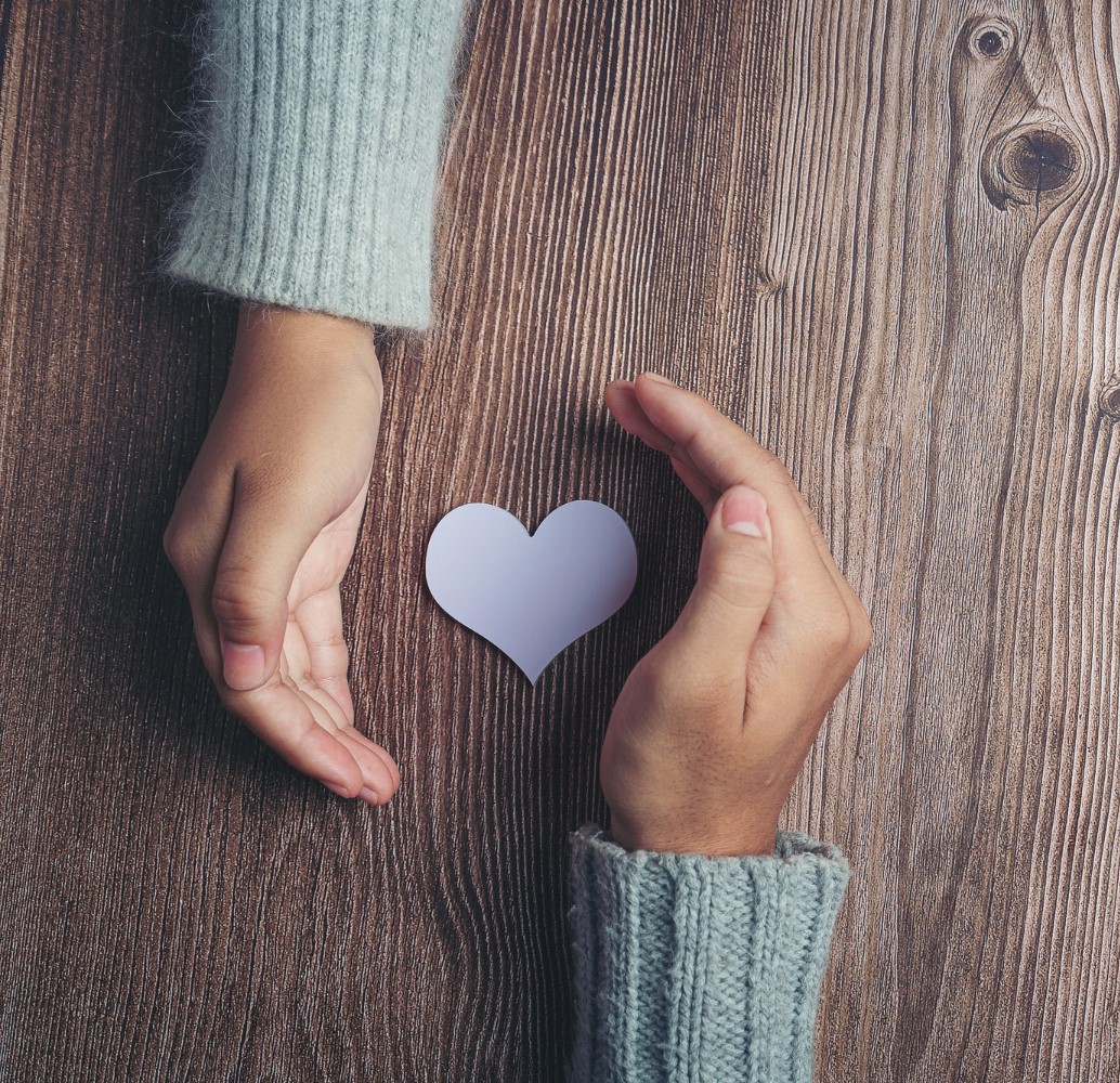 dłonie obejmują papierowe serce
