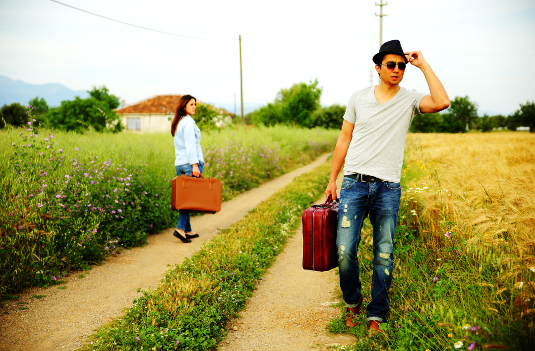 Dwie osoby z walizkami idące w inne strony polną drogą.