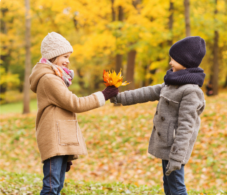 Dwoje dzieci przekazujących sobie jesienne liście