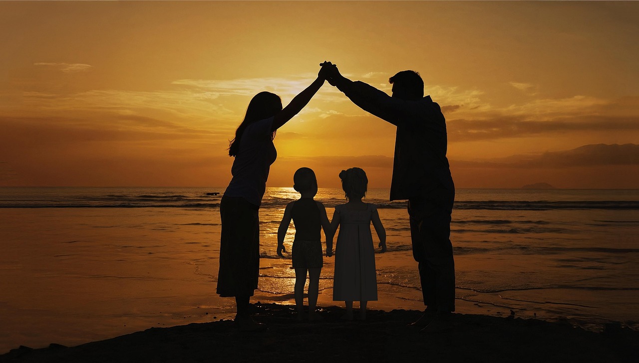 Rodzina z dwójką dzieci na tle zachodzącego słońca składające ręce nad głowami dzieci w kształcie domu